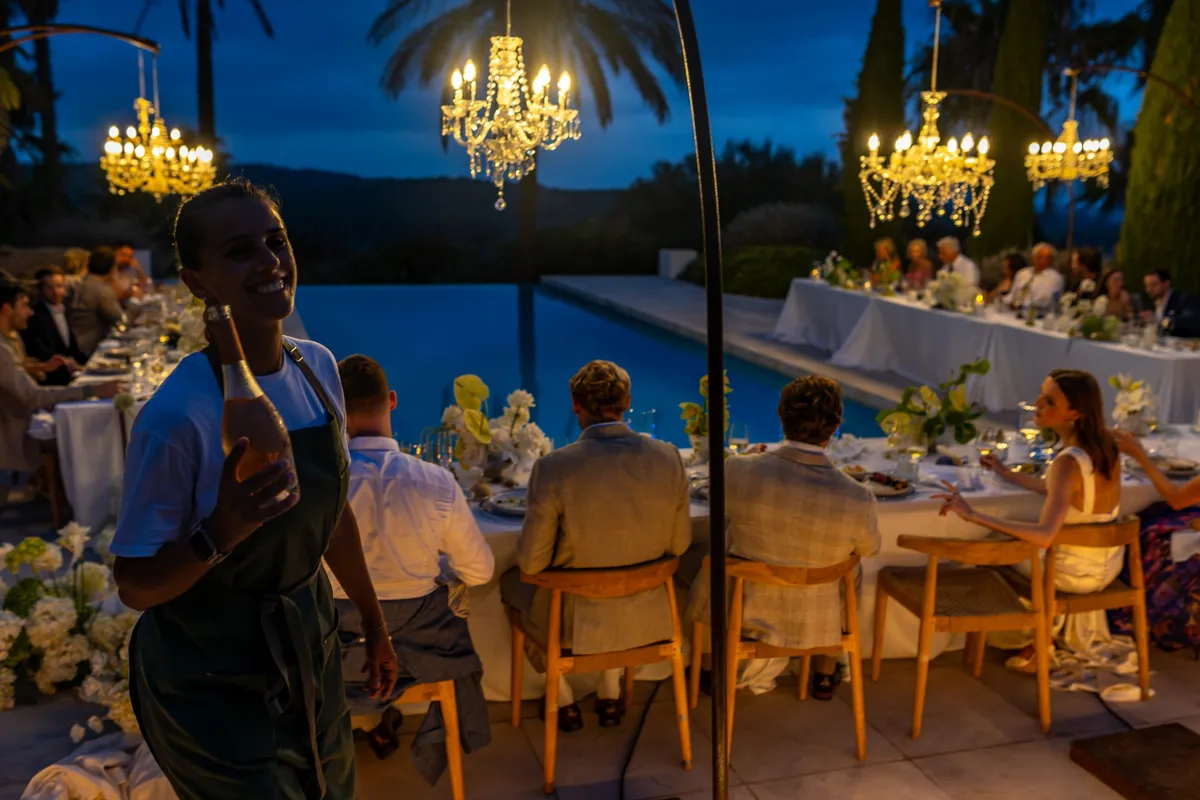 Camarera de Grupo Picolín sirviendo vino en una cena de boda junto a la piscina, bajo lámparas de araña