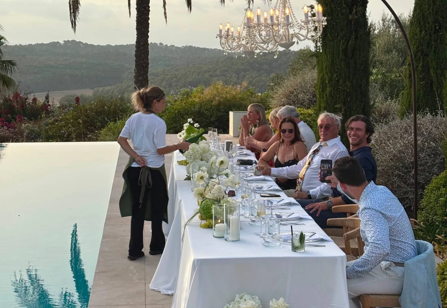 Camarera de Grupo Picolín sirviendo una cena junto a la piscina de una villa, bajo una lámpara de araña