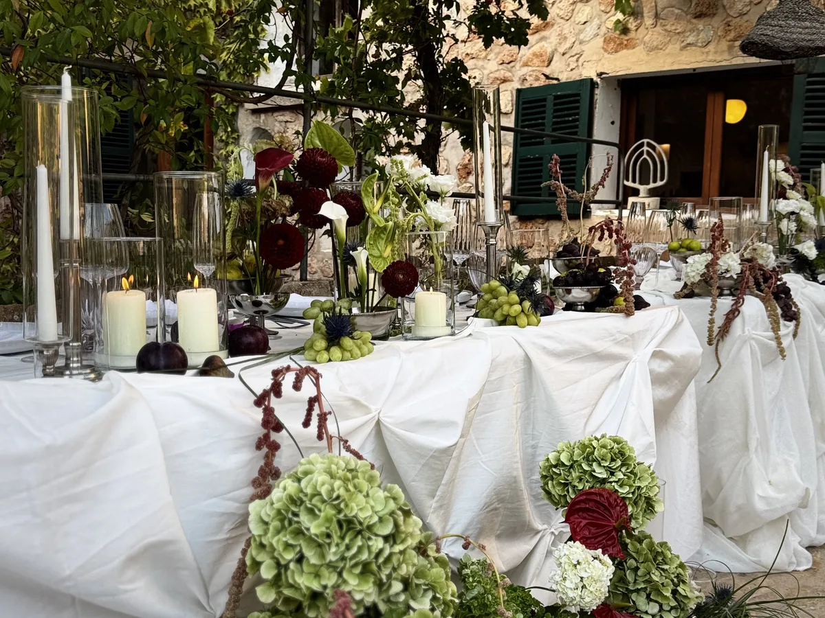 Hochzeitstafel mit Kerzen und Blumen unter einer Weinlaube an einem Steinhaus