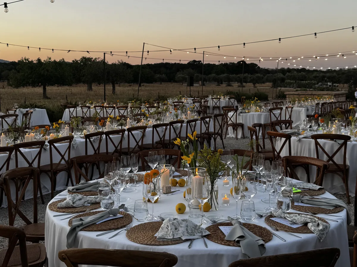 Hochzeitsbankett bei Sonnenuntergang auf einer Finca, mit runden Tischen und Lichterketten