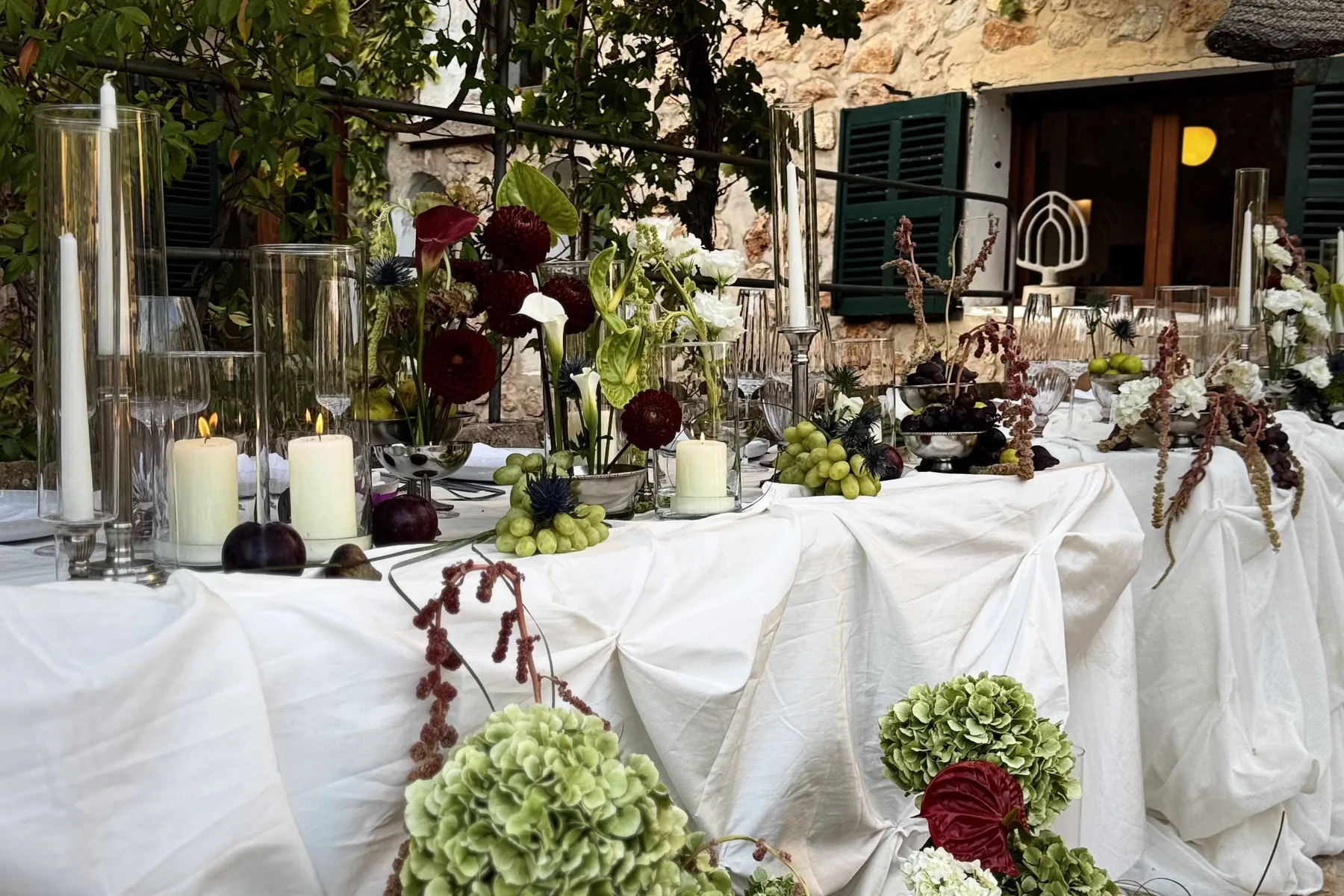 Festtafel mit Kerzen und Blumen unter einer Weinlaube an einem Steinhaus