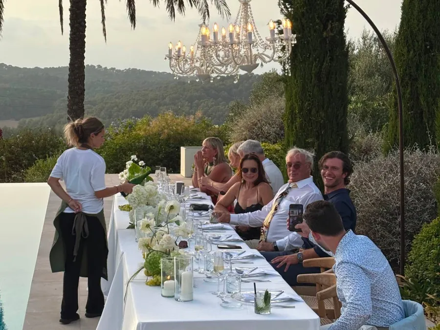 Camarera sirviendo una cena junto a la piscina de una villa, bajo una lámpara de araña