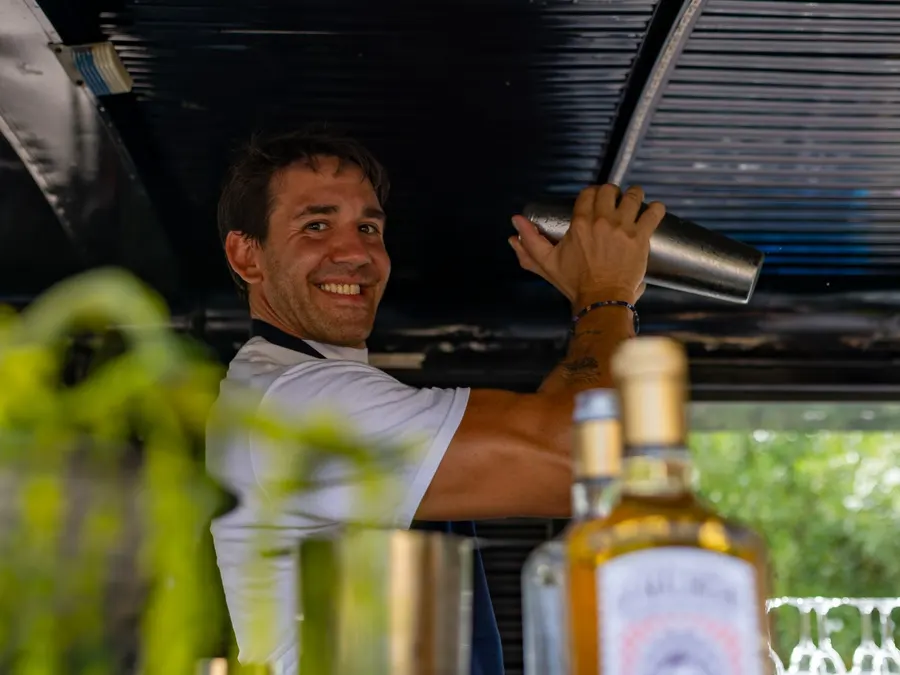 Coctelero sonriendo mientras agita la coctelera en la barra